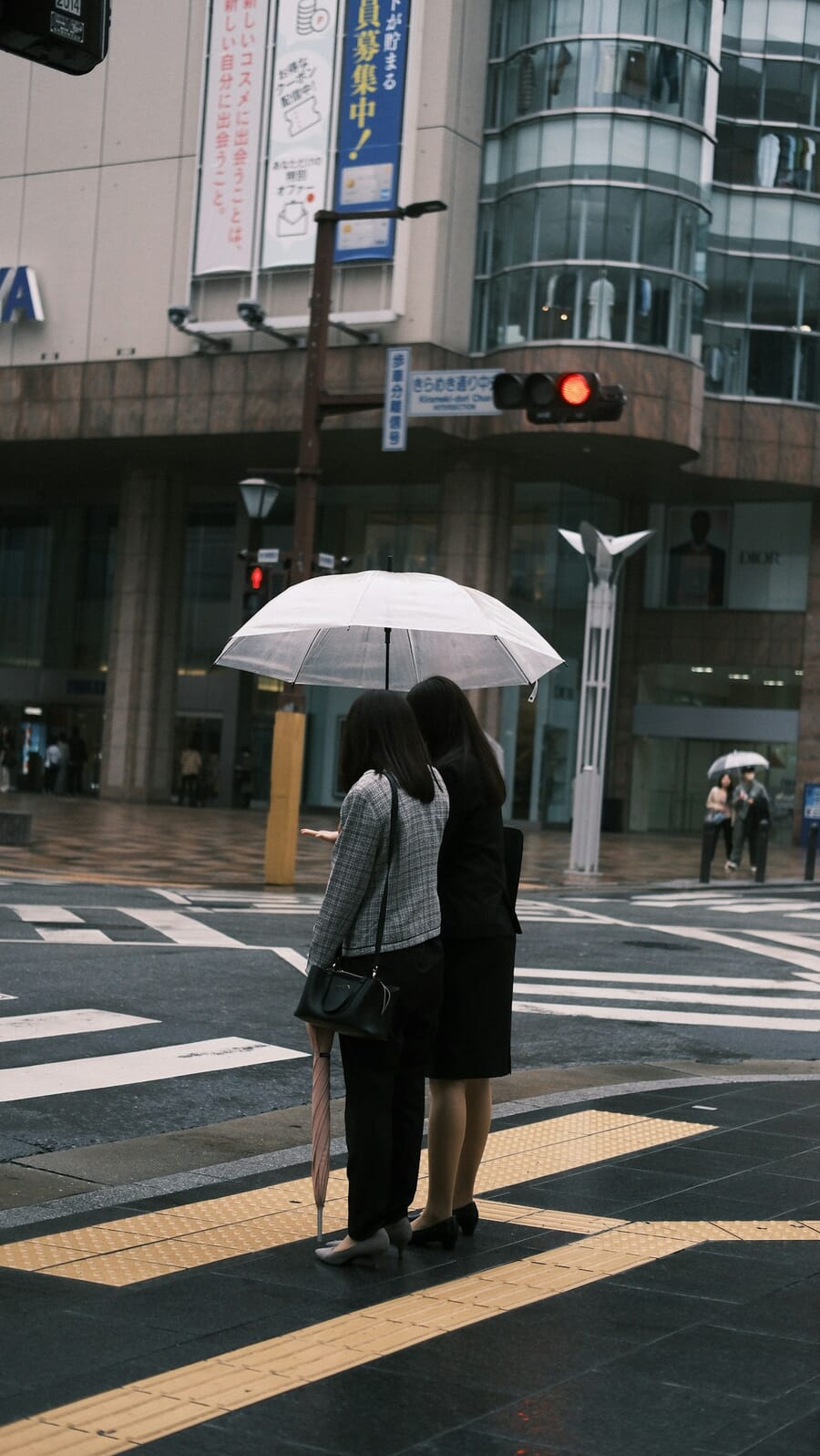 Two women sharing an umbrella at a rainy crosswalk — weather adds mood and graphic elements to urban photography