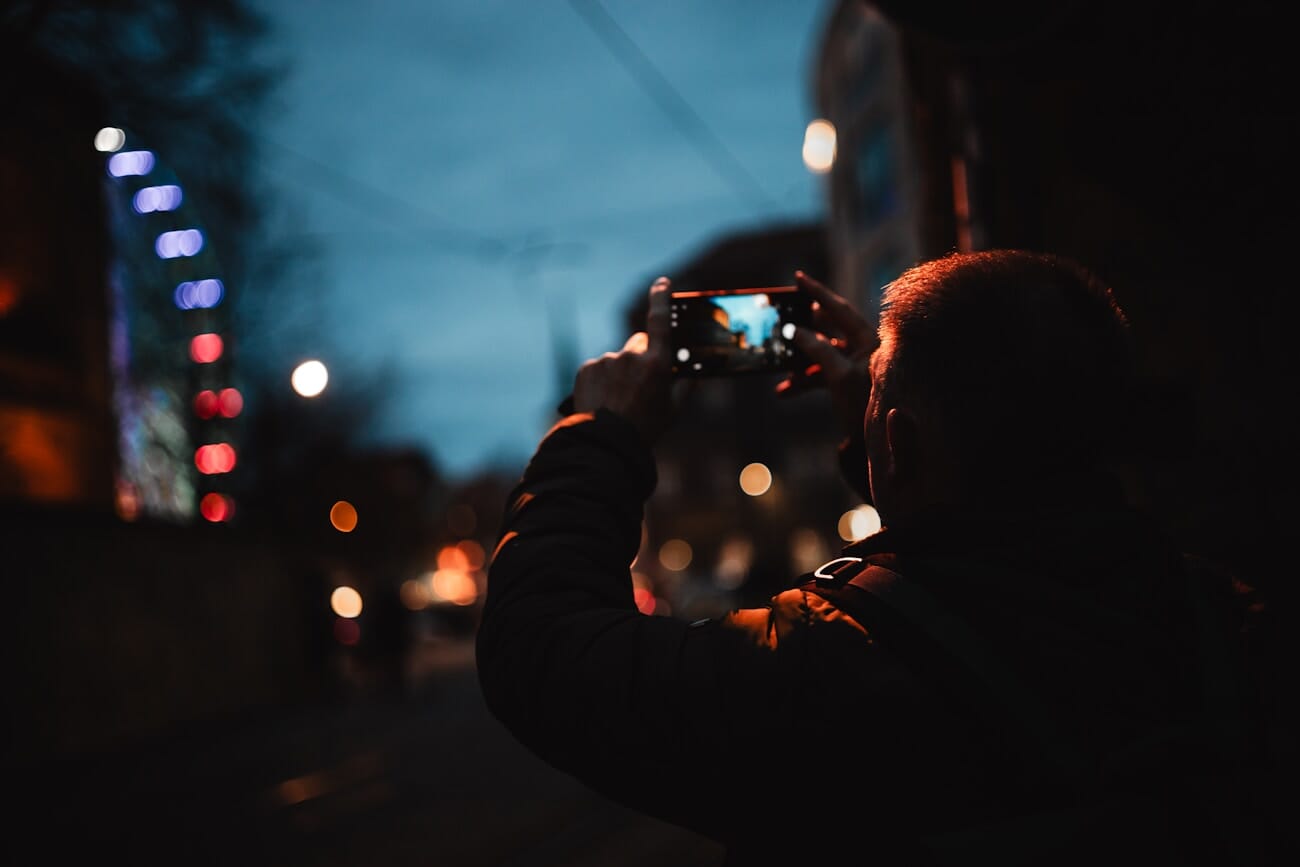 Man using smartphone camera at night with bokeh city lights in background