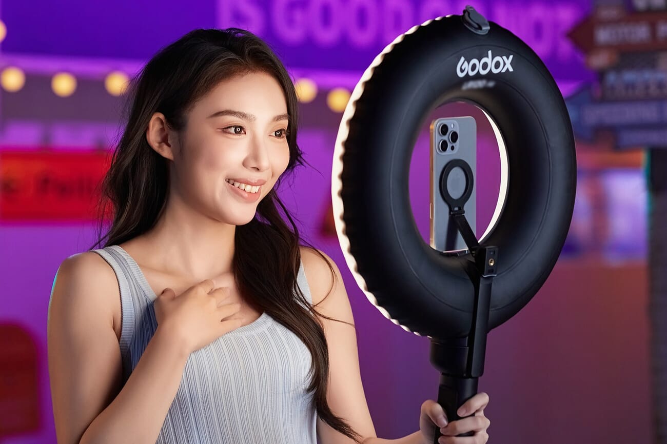 A creator holds the Godox LR150 Air inflatable ring light, which is lit up, in a colorful setting