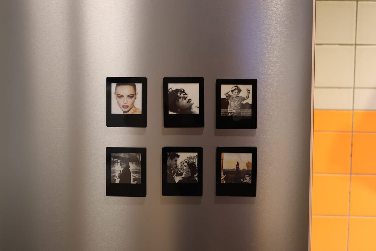 Six black Vidabay Snap E-Ink magnets arranged on a stainless steel fridge, each showing a different black-and-white photo
