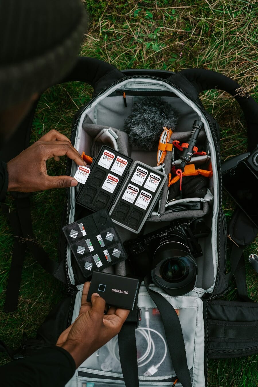 Camera field kit laid out in a backpack with memory cards, cables, and a compact camera, vertical composition