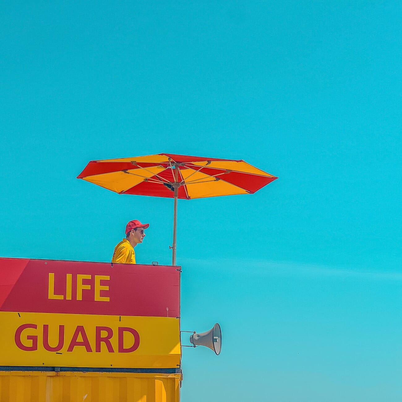 Lifestyle category winner, a lifeguard under a striped umbrella against a teal sky by Bertram Greenhough