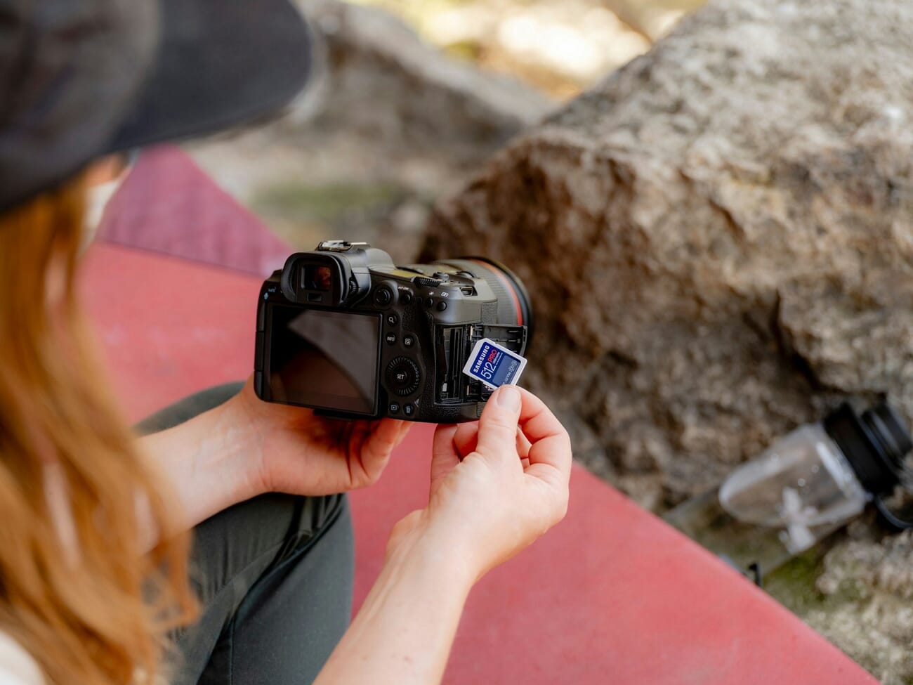 Photographer inserting an SD card into a mirrorless camera outdoors