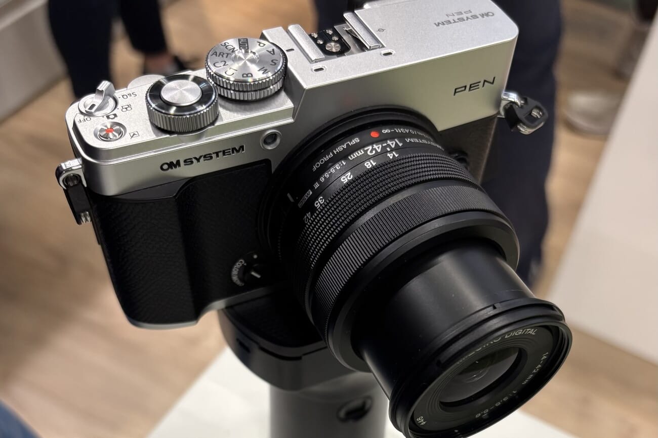 OM System PEN hands-on at a trade show: retro silver top plate, mode dial set near ART, and the extended M.ZUIKO 14-42mm splash-proof kit lens