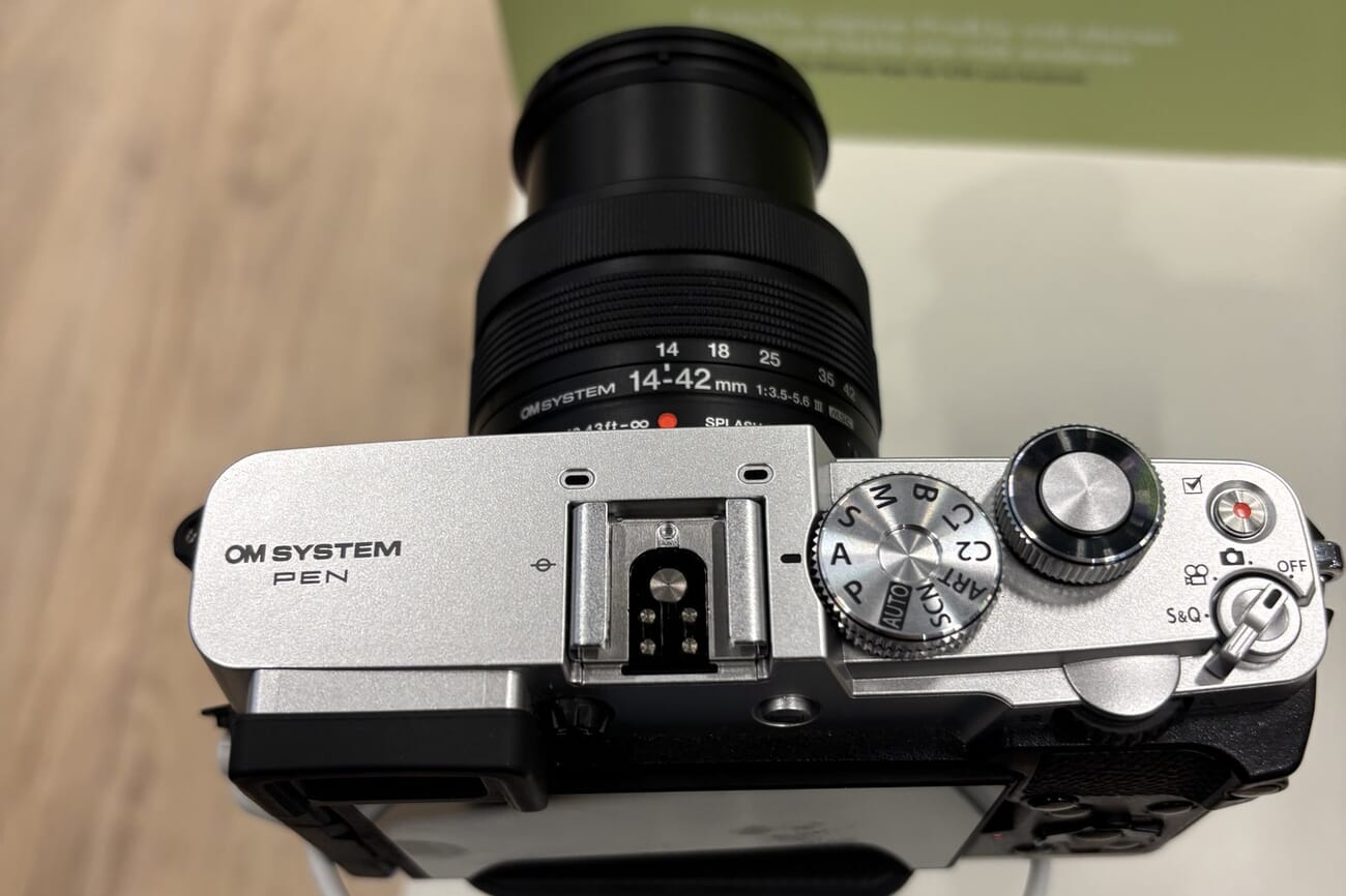 Top-down view of the OM System PEN in person, showing the retro control dials, hot shoe, mode dial with ART and SCN positions, and the stills, video and S&Q switch