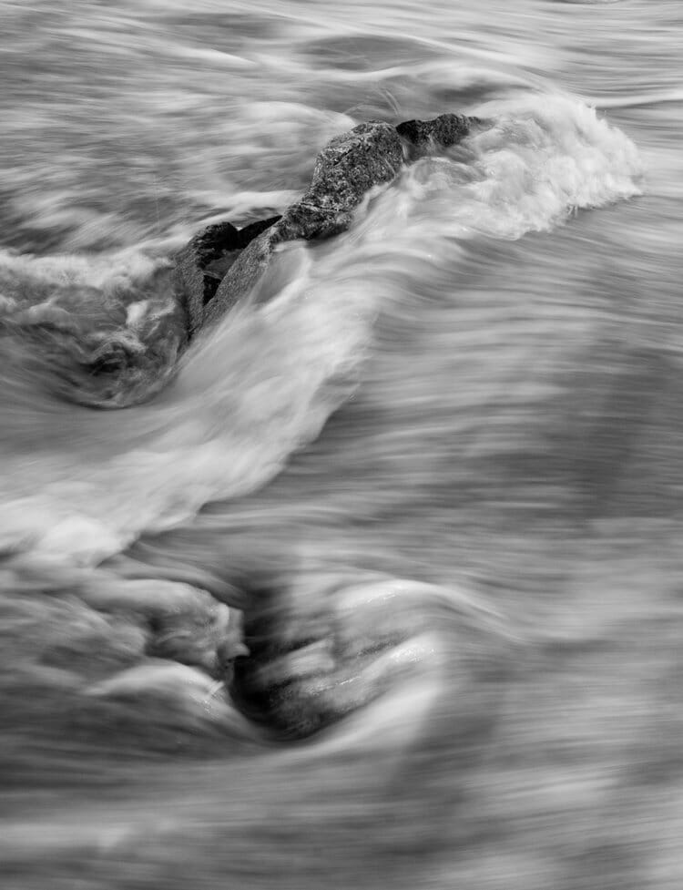Long exposure of rocks on a beach with blurry moving waves in black and white.