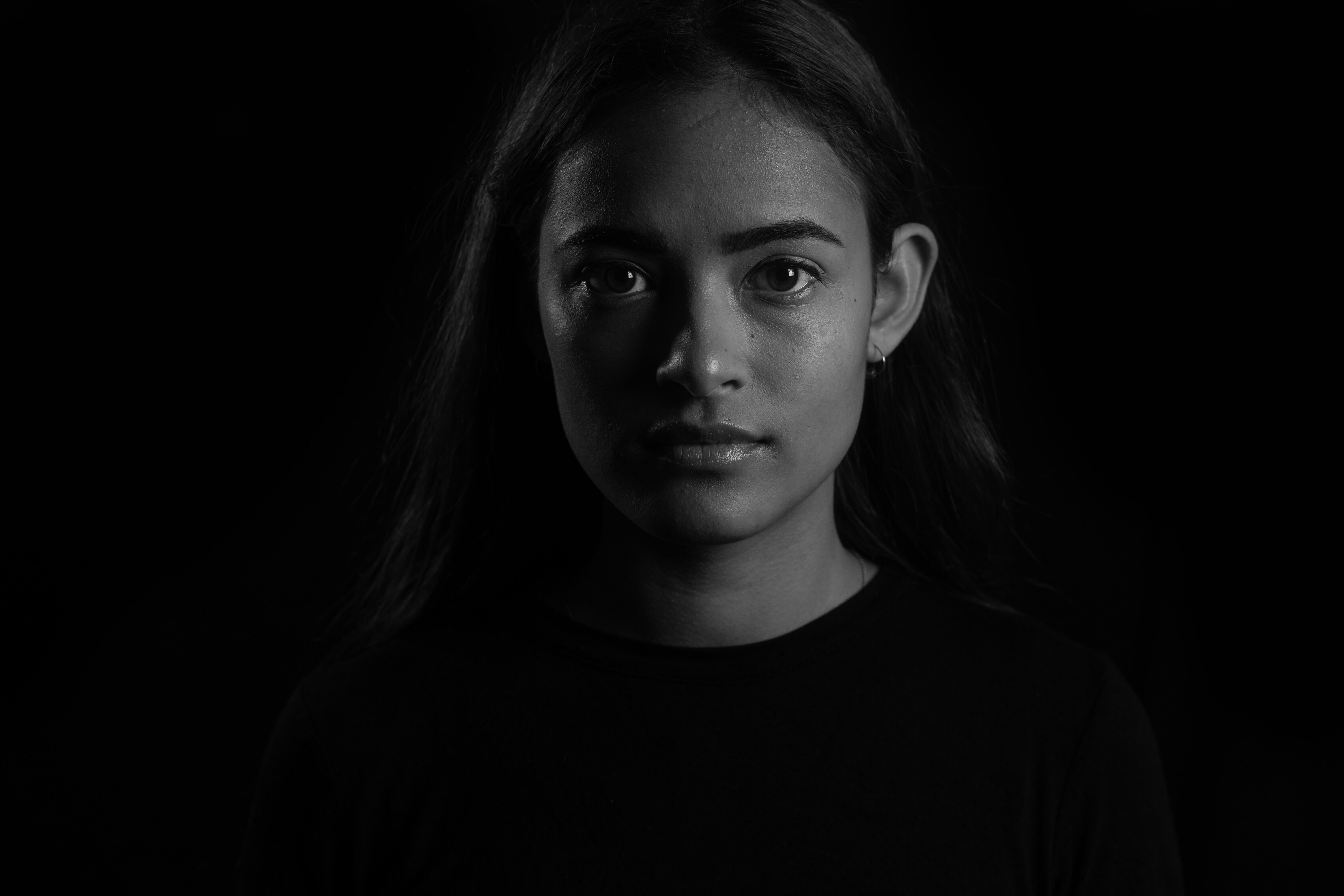 A striking black-and-white portrait of a young woman, showcasing sharp contrast against a dark background, ideal for exploring techniques in external flash.