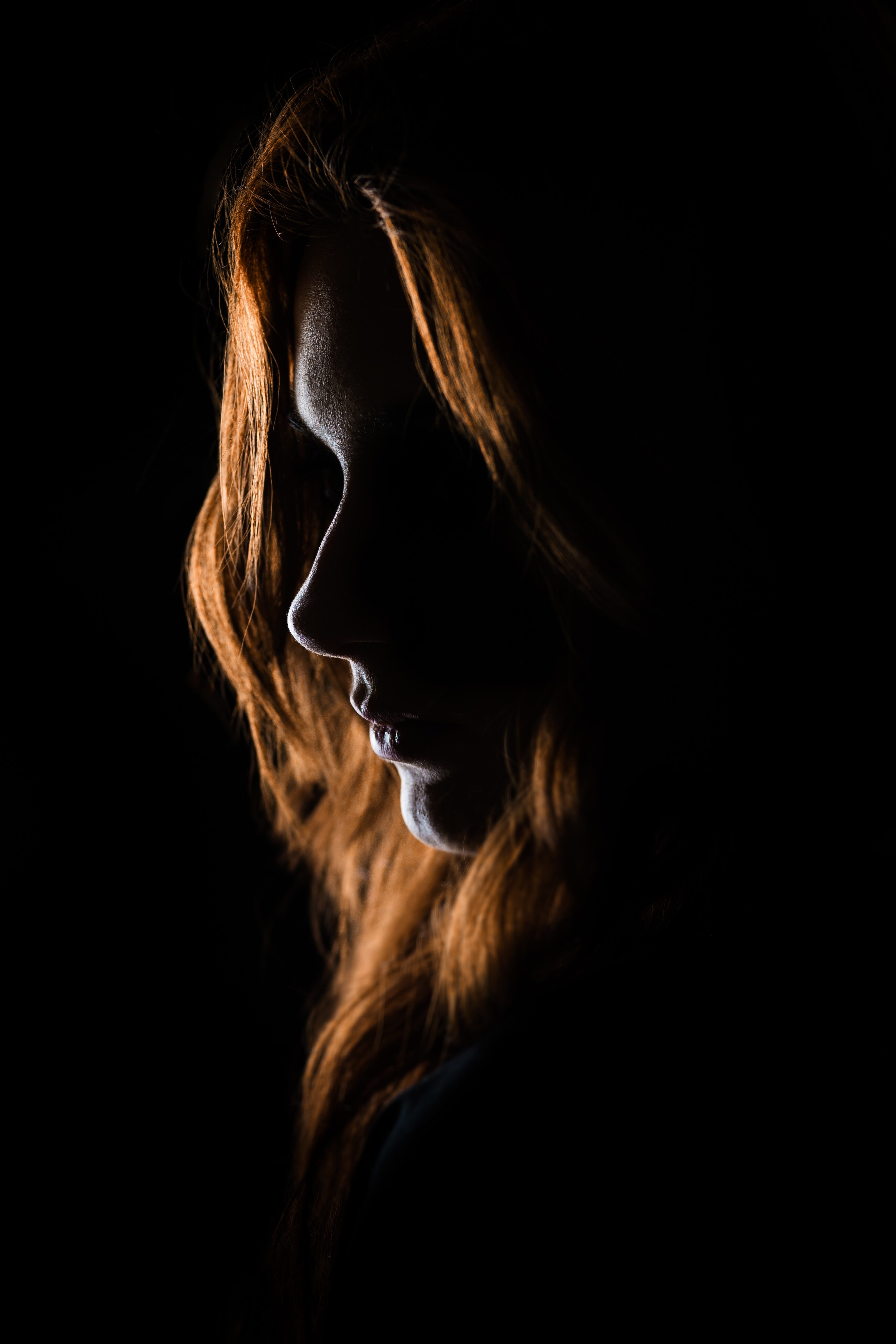 A dramatic silhouette of a woman with flowing red hair set against a dark background, highlighting the interplay of light and shadow in portrait photography. Perfect for exploring external flash.