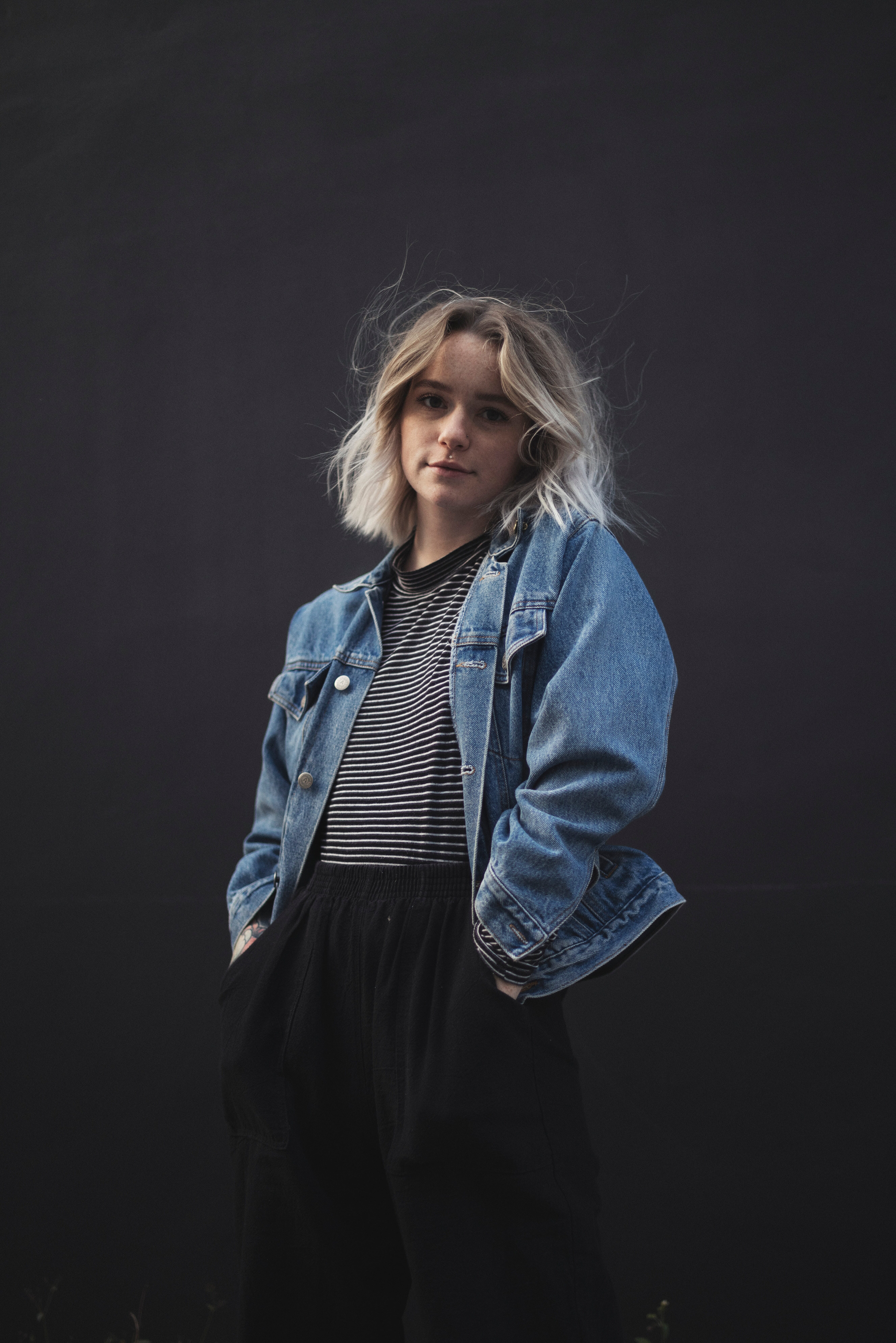 A stylish young woman poses against a dark background, wearing a denim jacket over a striped shirt, showcasing a relaxed and modern aesthetic perfect for exploring external flash techniques in.