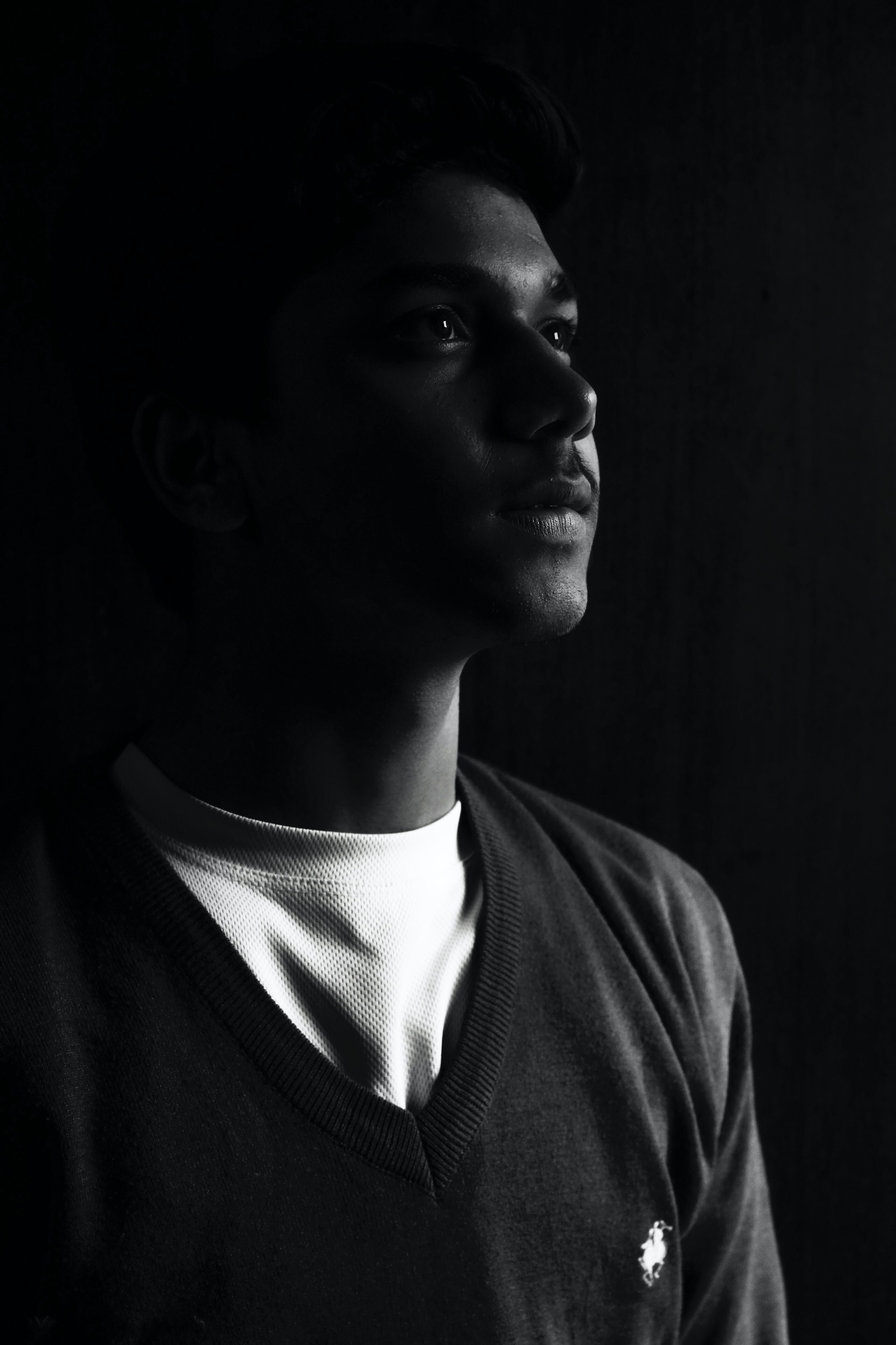 A striking black-and-white image featuring a young man's profile, illuminated dramatically against a dark background, highlighting facial features and conveying a contemplative.