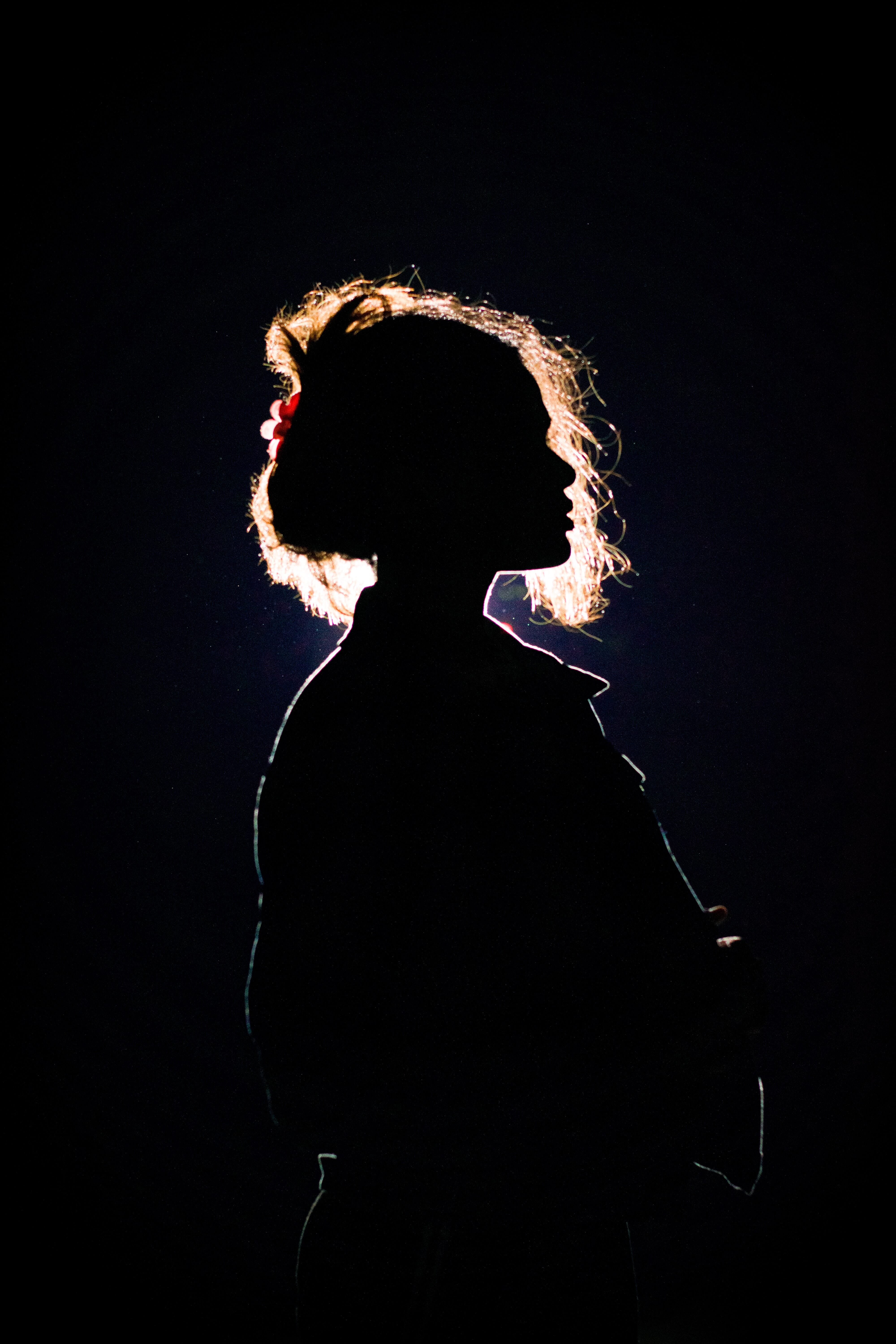 Silhouette of a woman against a dark background, illuminated by external flash. The light highlights her curly hair and profile, demonstrating effective flash use in.