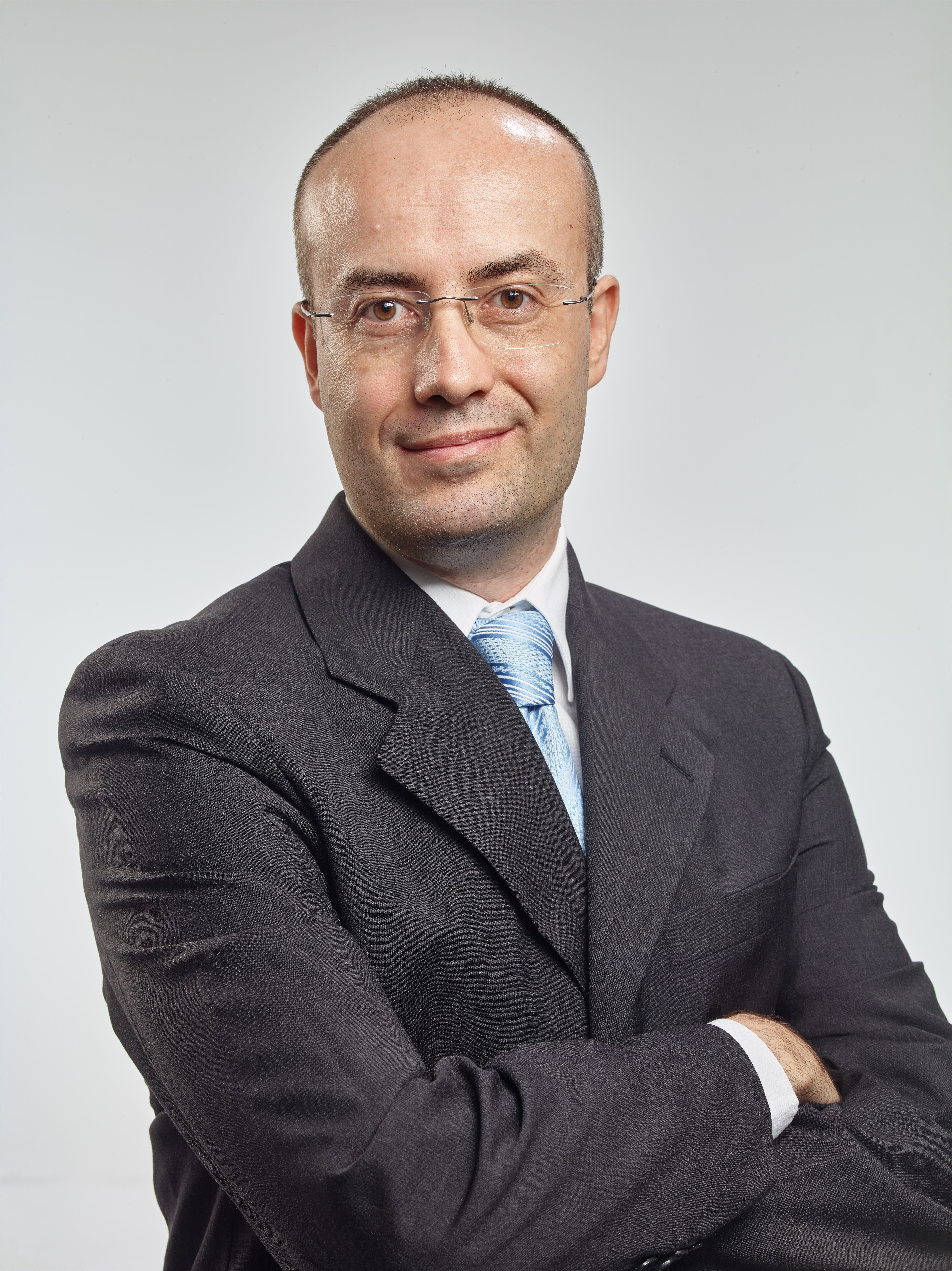 Head and shoulders of a man with glasses and a gray suit looking straight ahead.