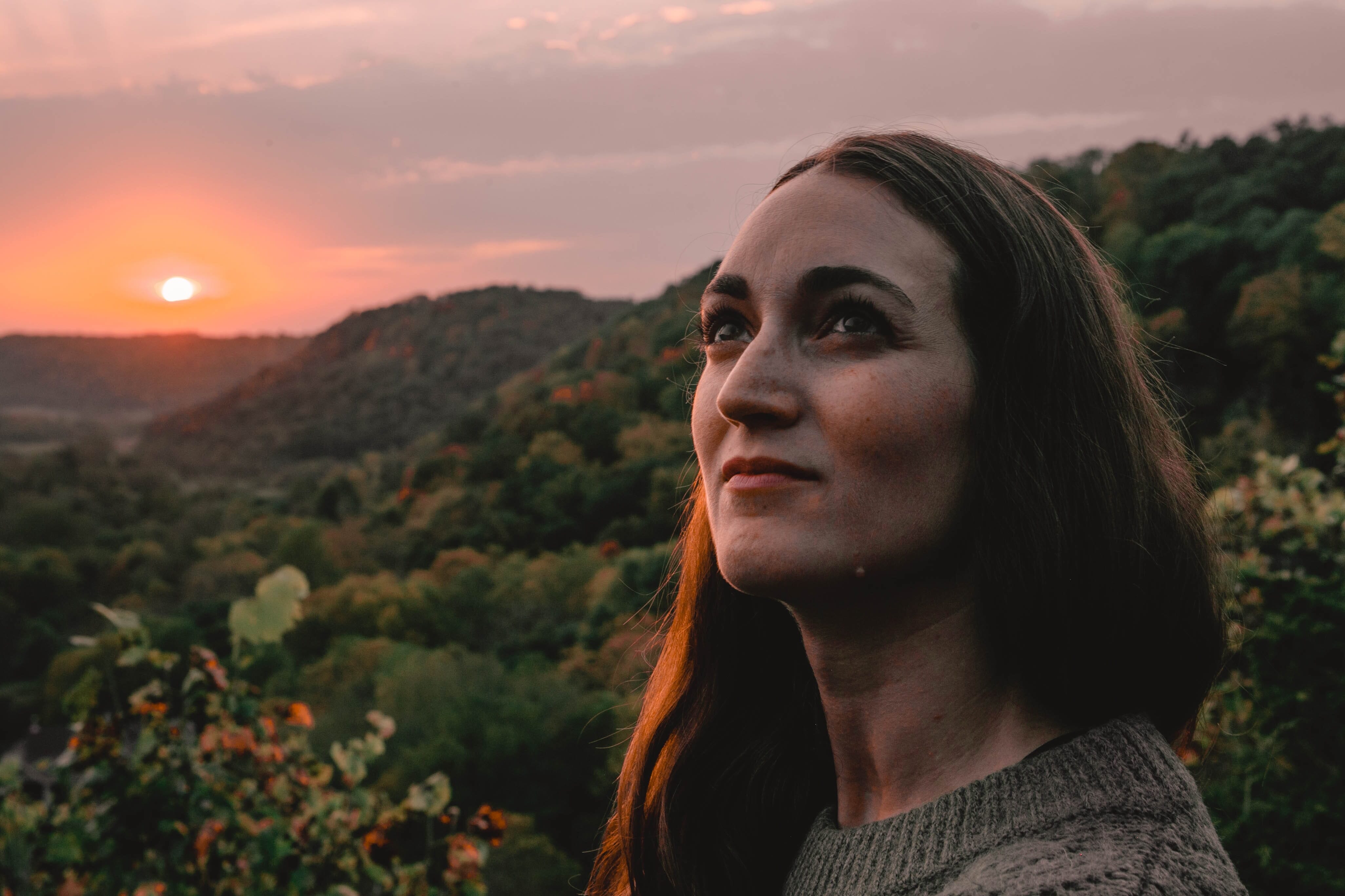 A woman gazes at a sunset over lush green hills, showcasing warm golden light and soft shadows perfect for captivating portrait.