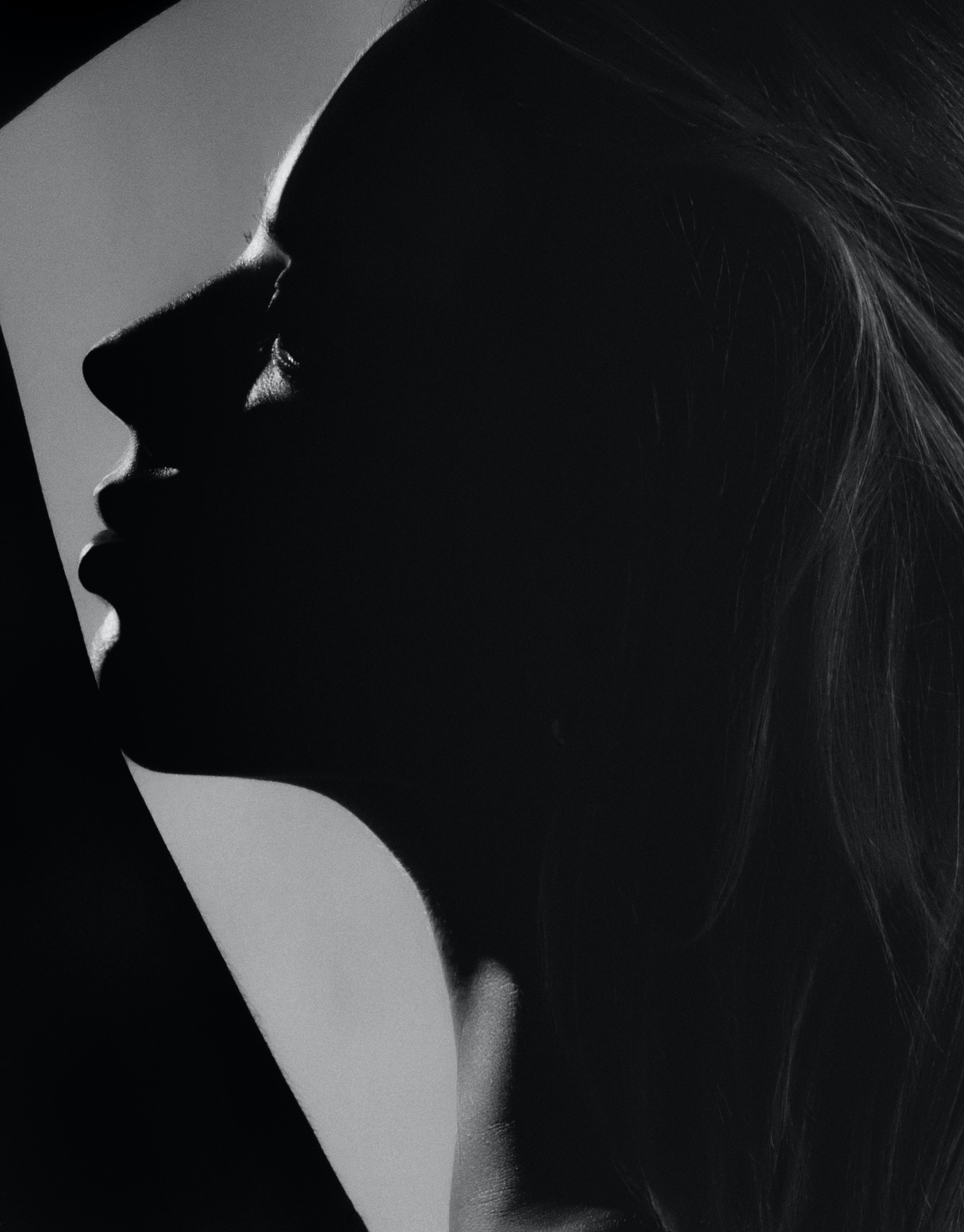 A dramatic black and white portrait highlights a profile with soft lighting. The silhouette showcases defined features and flowing.