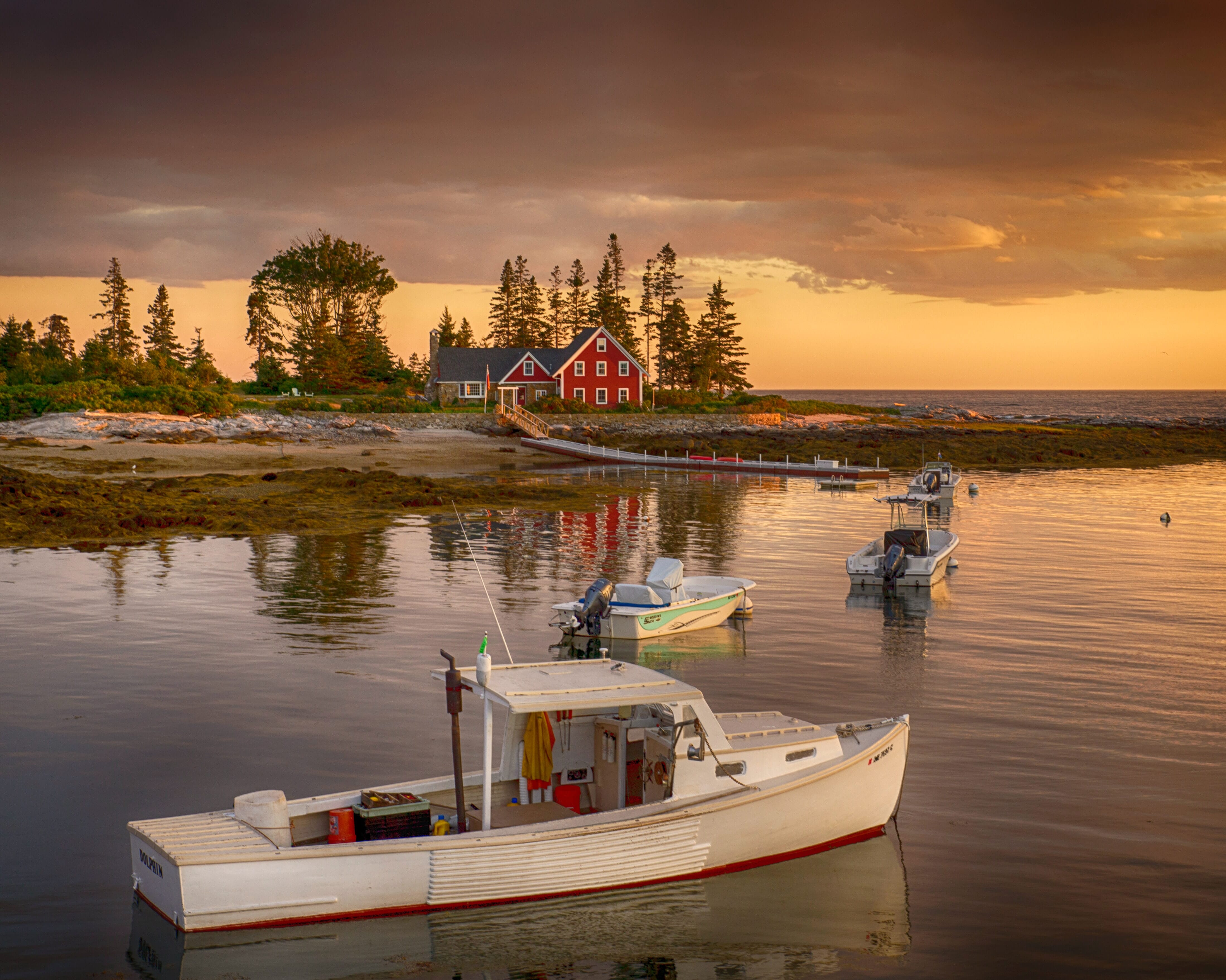 Sunset with a boat on a lake before a red house.