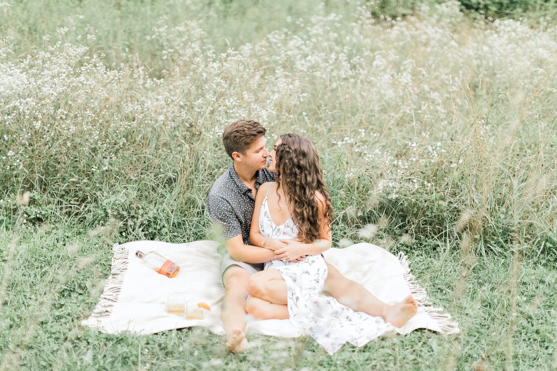 man and woman kissing on blanket in a meadow