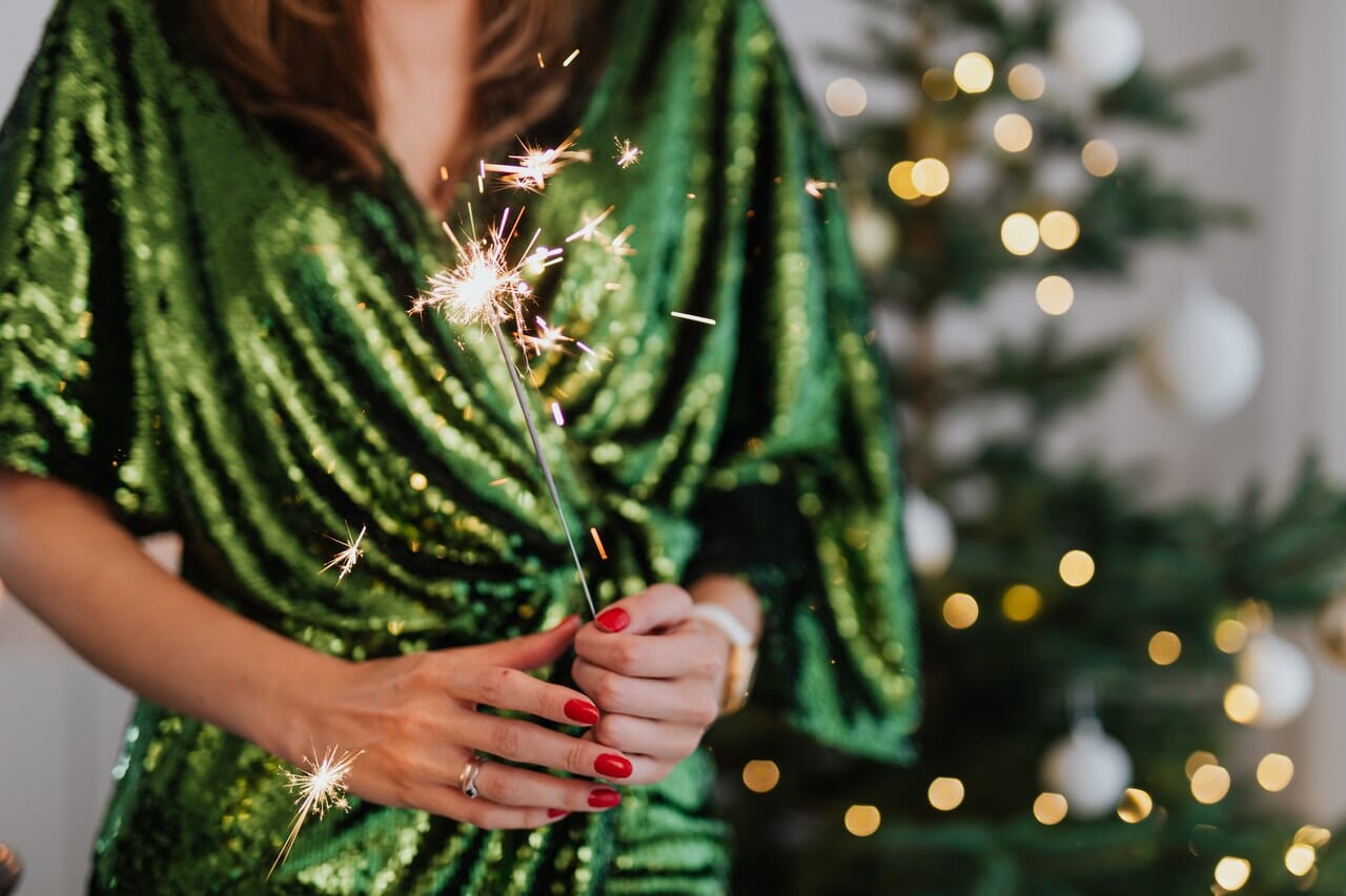 Woman dressed in green holding a lit sparkler with a Christmas tree in the background.