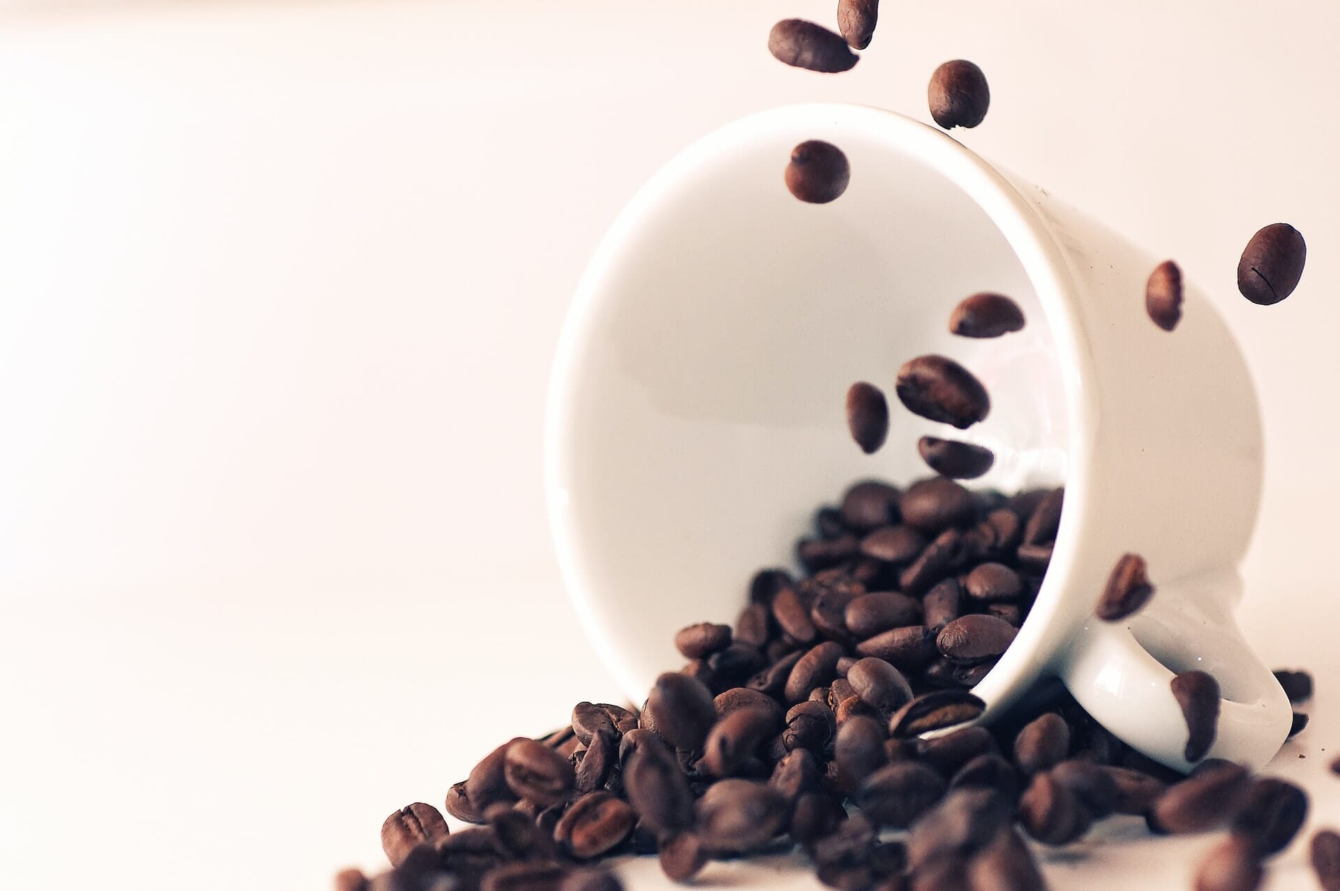 Freeze motion image of falling coffee beans and white coffee cup