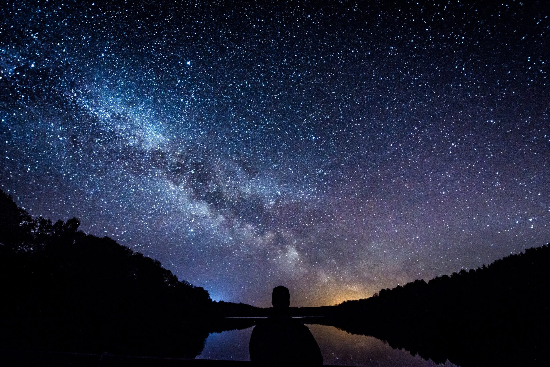 Starry skies with man in silhouette in foreground.