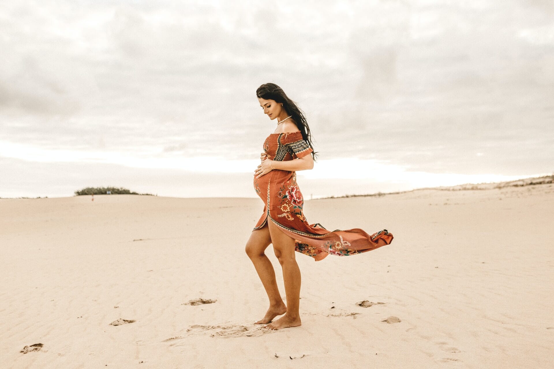 Pregnant woman walking on beach.