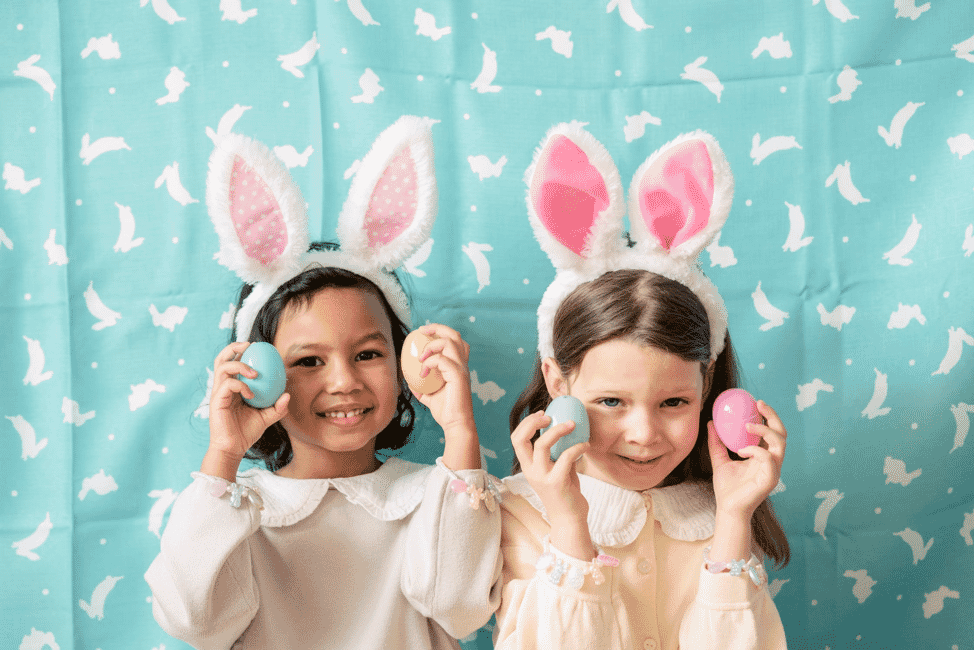 Two little girls wearing rabbit ears and holding Easter eggs