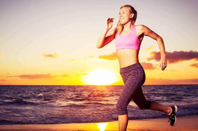 Woman running on beach with sun in background.