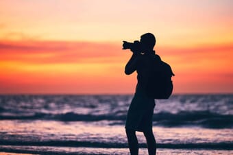Silhouette of a man with a camera photographing on a beach at sunset.