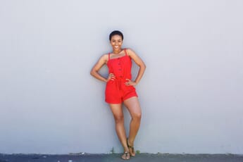 Full body portrait of a woman in red clothing standing against a gray wall outdoors while smiling