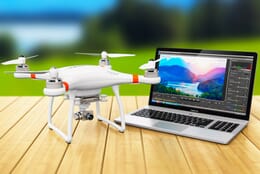 A white drone and a Macbook laptop on a wooden table.