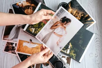 Hands holding photograph of woman in white dress above pile of photos on table