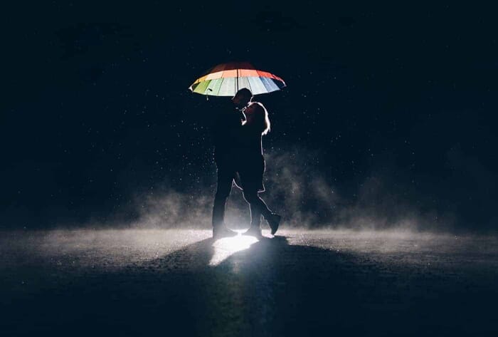A silhouette of a couple under an umbrella in the rain at night.
