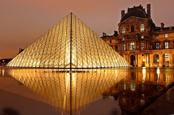 The Louvre Pyramid with reflection in water at dusk in Paris