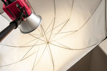 Red studio strobe firing into mounted white umbrella.