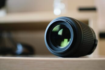 Close-up of a black Nikon macro lens sitting on a table surrounded by background blur.