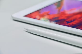 Close-up of the corner of a white tablet and a tablet pen on a gray surface.