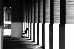 A roller chair sits at the end of a line of columns with light streaming through the gaps in black and white.
