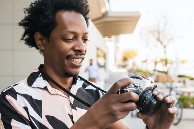 Man with a mustache smiling while viewing an image on the back of an old or retro-style camera.