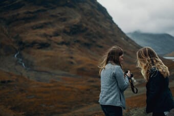 Two long-haired teen girls looking at a camera with mountains and fog in the background.