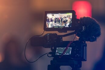 Video rig with camera, microphone, and field monitor showing group of people at a party