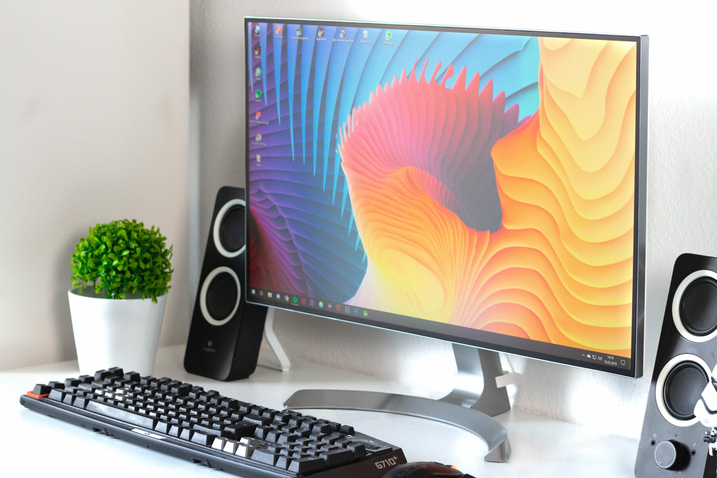 Desk setup with plant, keyboard, speaker, and monitor for photo editing displaying a colorful background