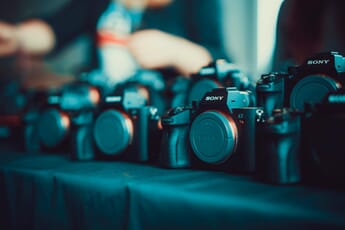 Sony a7R mirrorless cameras with body caps sitting in a row on a cloth surface.