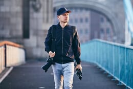 Man carrying a camera and a tripod without a bag.