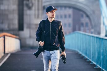 Man carrying a camera and a tripod without a bag.