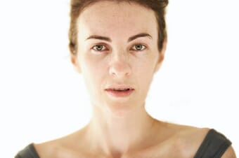 Woman with short brown hair looking straight ahead with her mouth slightly open framed by a white background.