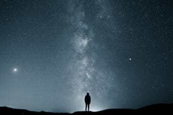 Man standing on hill at night watching the stars.
