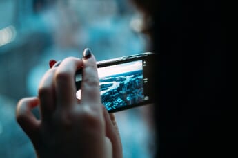 Woman's hands with painted fingernails holding a smartphone with its camera open and showing a cityscape.
