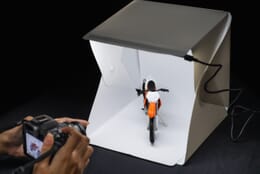 Lightbox lit up with toy motorcycle inside while photographer takes picture.
