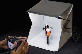 Lightbox lit up with toy motorcycle inside while photographer takes picture.