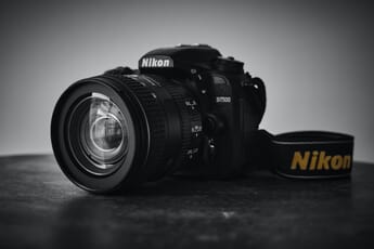 Nikon D7500 camera on a dark surface with a white background and a zoom lens attached.