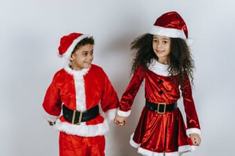 Girl and boy holding hands while dressed in red Santa outfits.